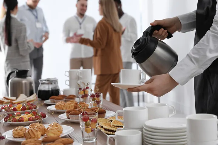 Breakfast setup with coffee, tea, pastries, and professionals networking in the background at a corporate event organized by Joyous Events